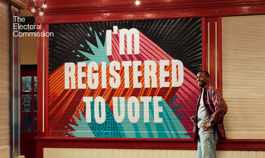 A wall with the text 'I'm registered to vote' and a person stood next to it smiling