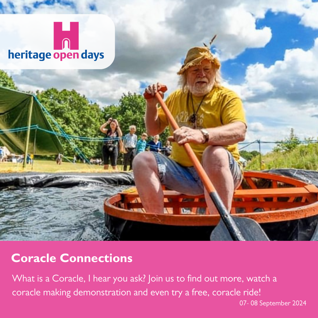 A man with a white beard in a yellow top and hat sat on a coracle boat with an oar in his hand on some water. There are people in the background watching on a blue sky, cloudy day.