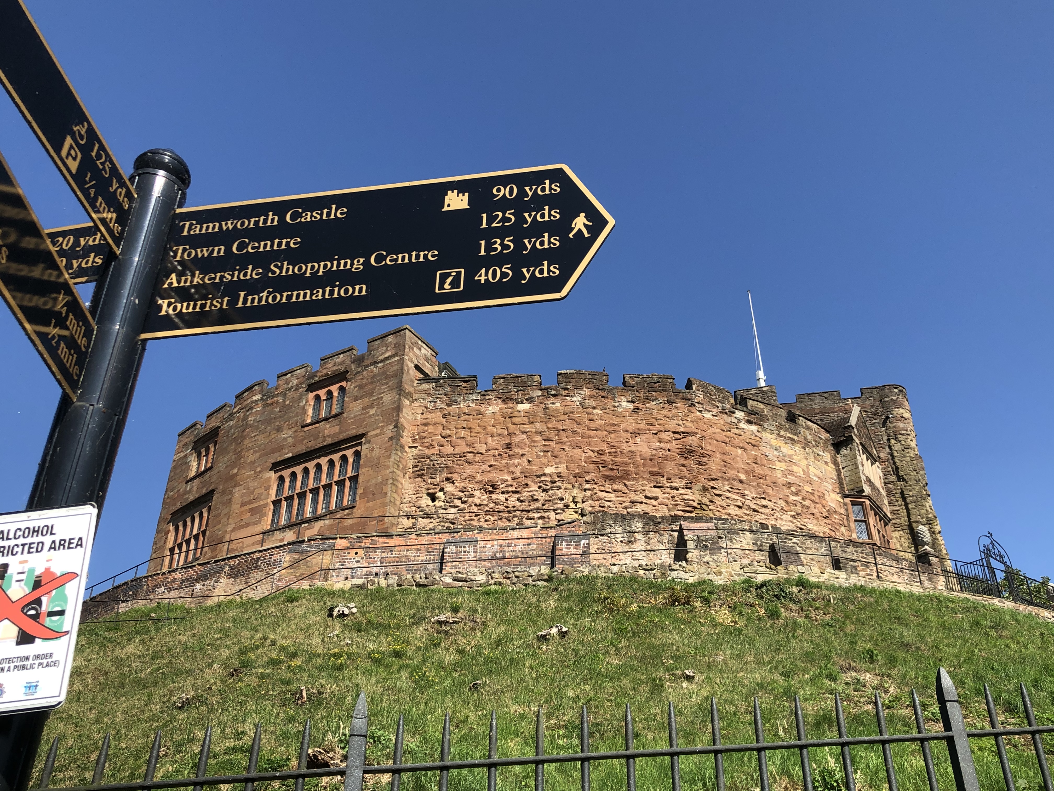 Tamworth Castle on a grassy hill. A signpost is in front of it.