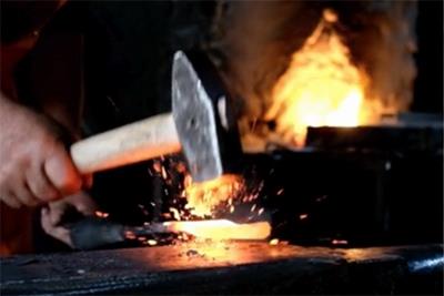 A hand holding a blacksmith hammer with a flat end in front of a fire