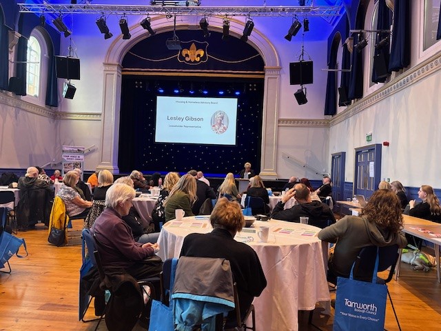 image of a room with a stage and screen and people sitting at round tables