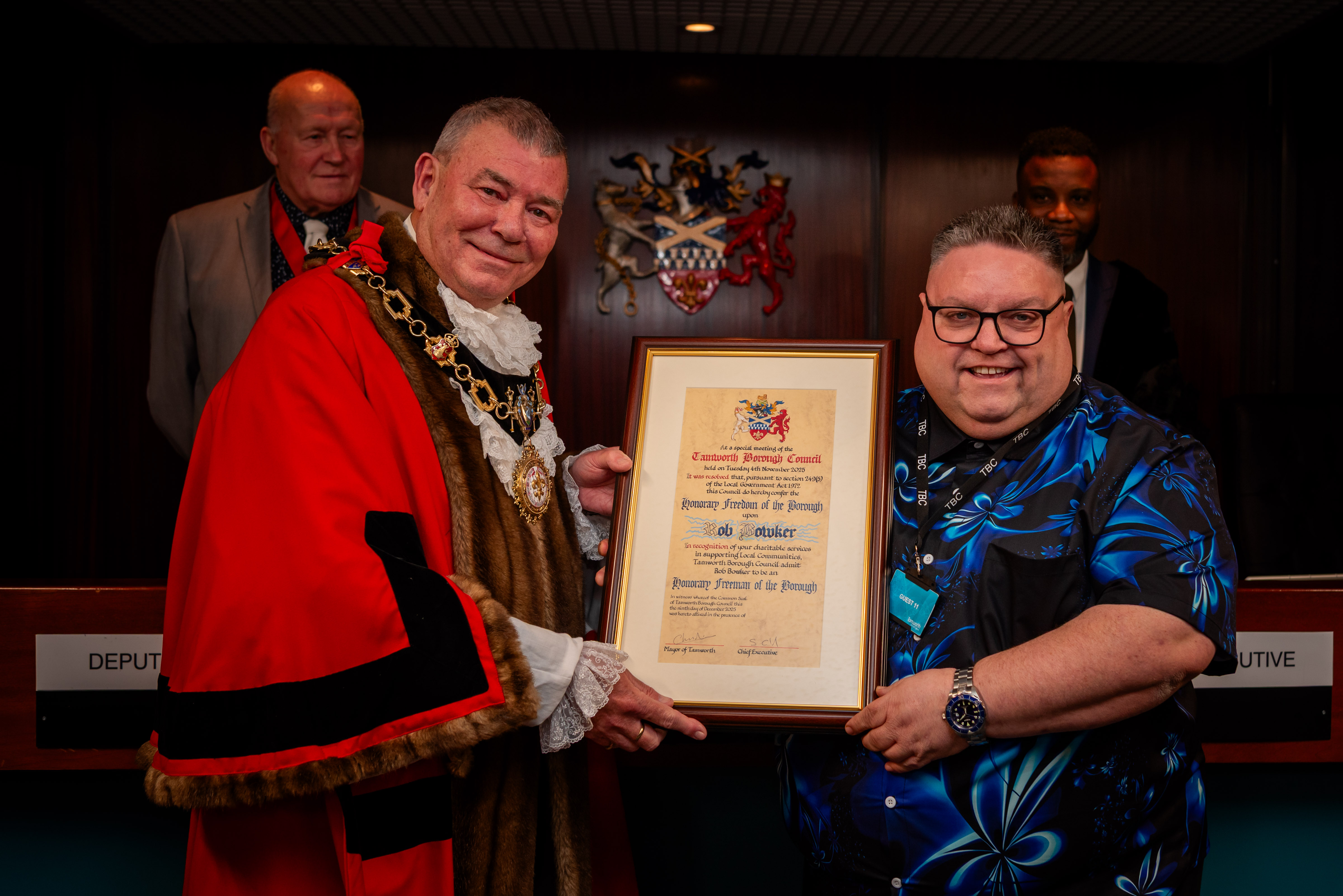 image of a male and mayor with red robes and chains, holding a certificate in a frame