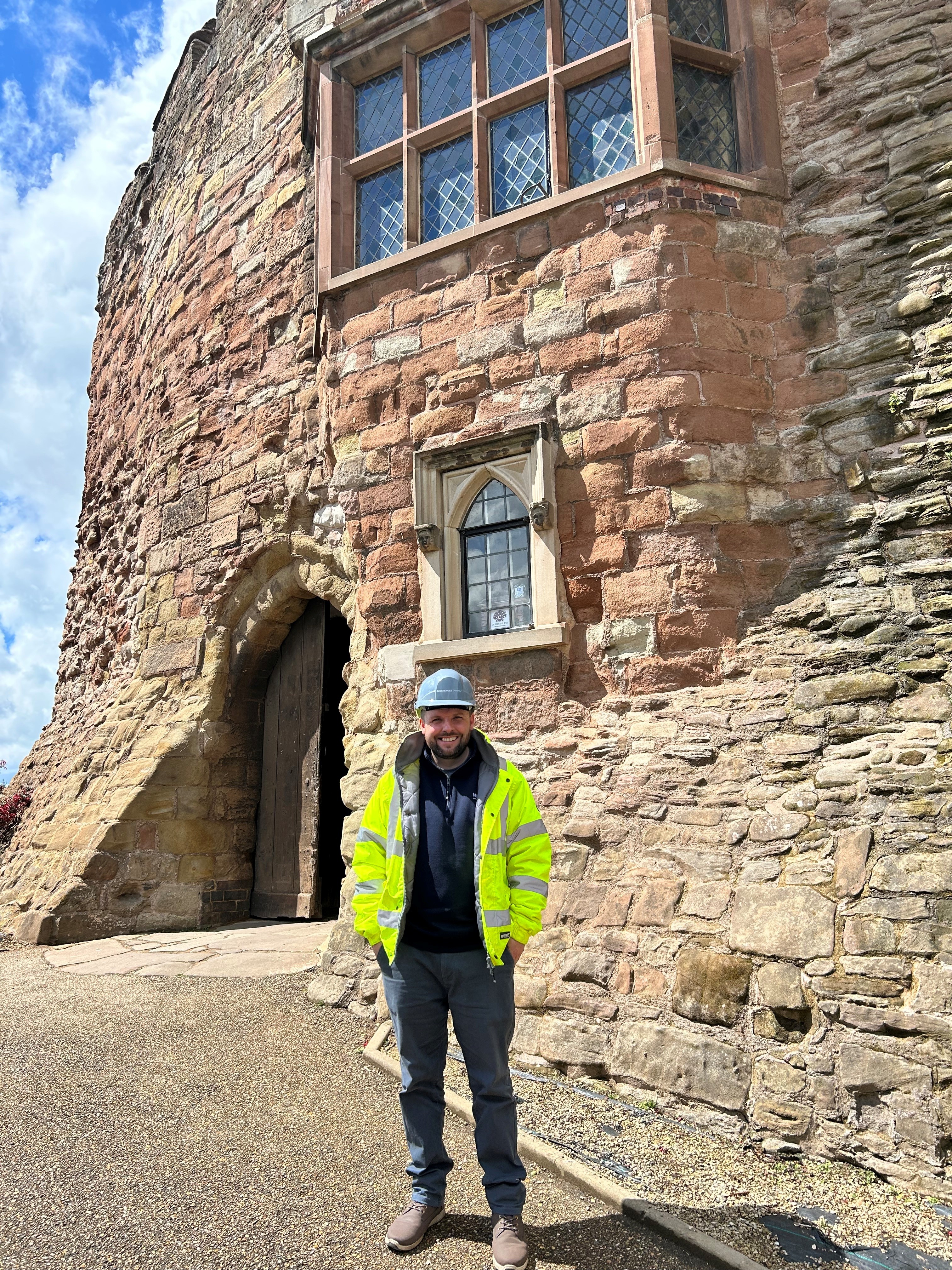 photo of a person wearing a hi vis jacket, hard hat outside the front of a castle building