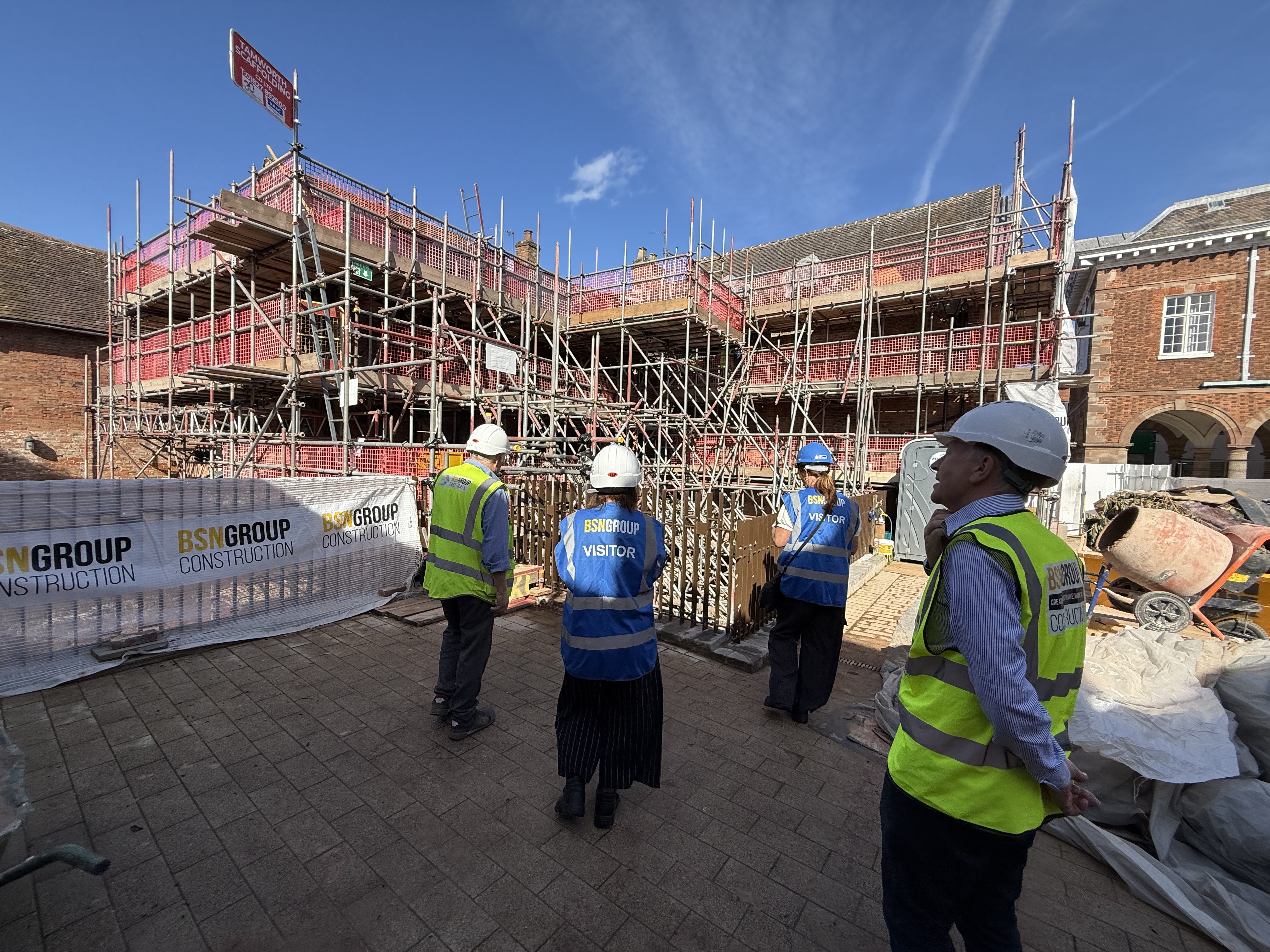 4 people in front of Market St properties in Tamworth with high vis and hard hats as the building is getting restored and has lots of complex scaffolding up around it.