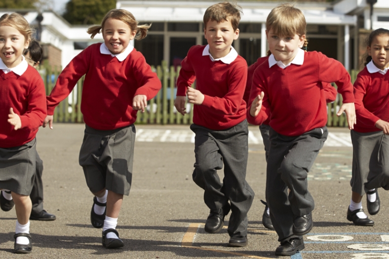 Five primary school aged children in red jumpers and grey trousers or skirts, running on a school playground. Please note this is a generic stock image.