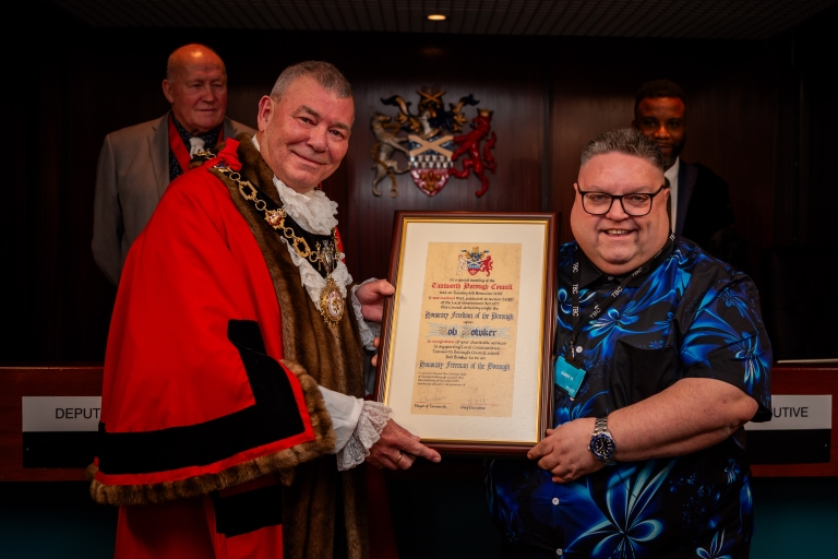image of a male and mayor with red robes and chains, holding a certificate in a frame