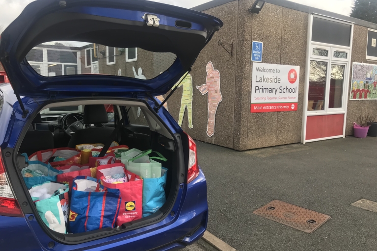 A car with its boot open with lots of bags full of hygiene products parked next to a building