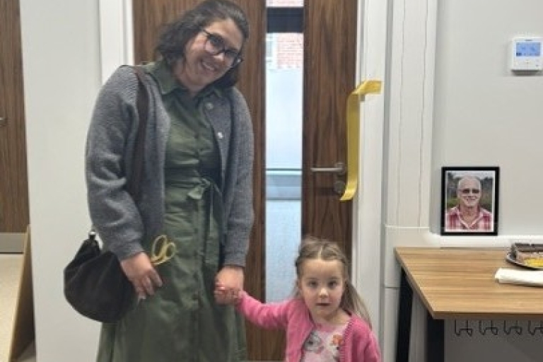 adult and small child standing by a door after cutting a ribbon