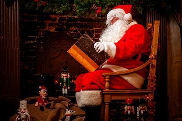 Santa sat on a chair by a fireplace reading a big book