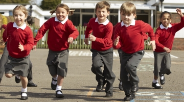 Five primary school aged children in red jumpers and grey trousers or skirts, running on a school playground. Please note this is a generic stock image.