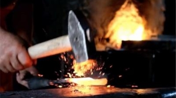 A hand holding a blacksmith hammer with a flat end in front of a fire