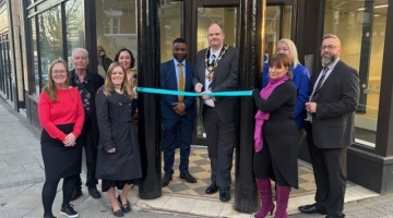 group photo outside a building with dark pillows, teal ribbon being cut