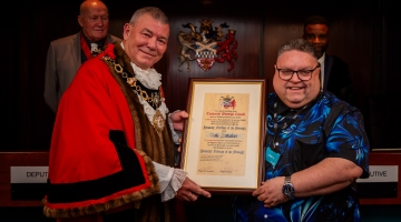 image of a male and mayor with red robes and chains, holding a certificate in a frame