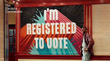 A wall with the text 'I'm registered to vote' and a person stood next to it smiling
