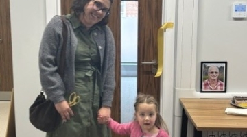 adult and small child standing by a door after cutting a ribbon