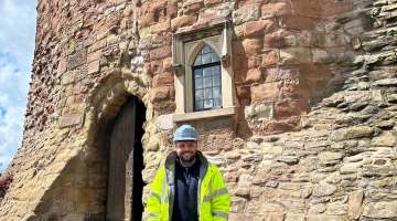 photo of a person wearing a hi vis jacket, hard hat outside the front of a castle building